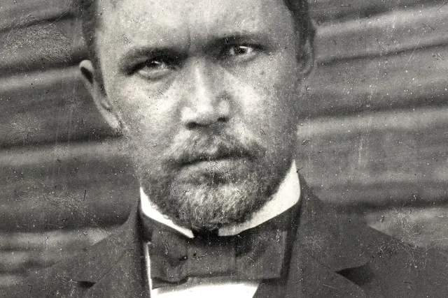 Mustavalkoinen valokuva nuoresta miehestä puvussa, katse suoraan kameraan.