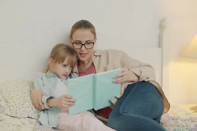 Aikuinen lukee kirjaa pienelle lapselle sängyssä